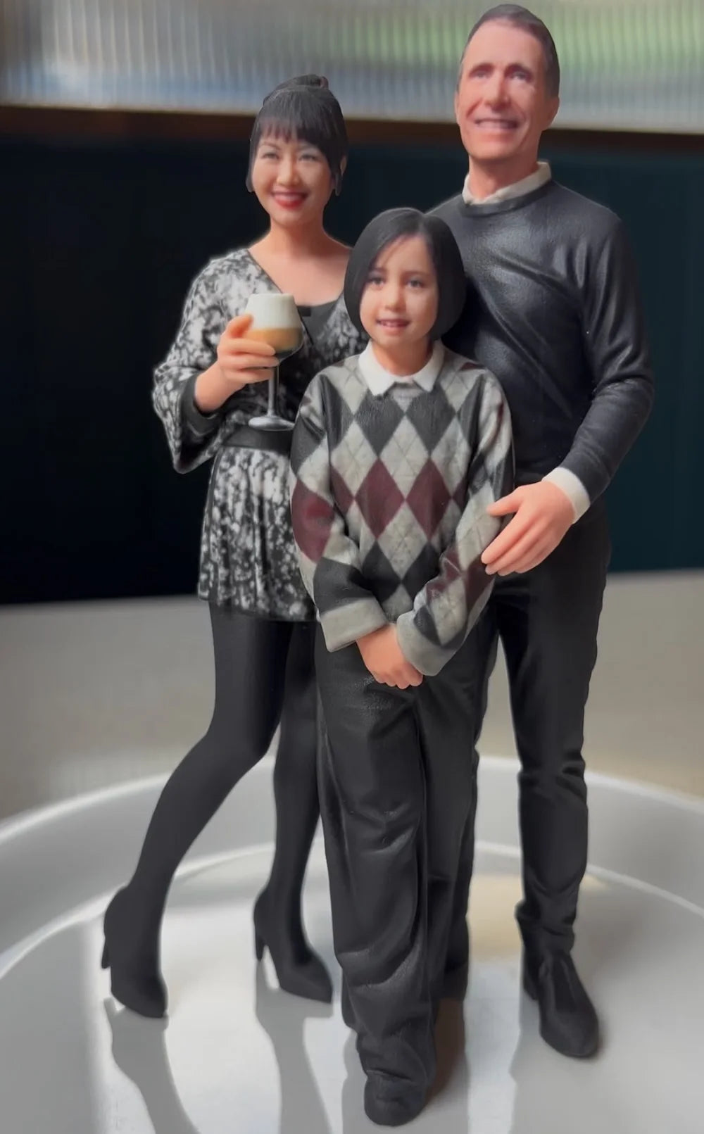 Front view of a custom 3D family figurine, mother holding champagne beside father and daughter in an argyle sweater