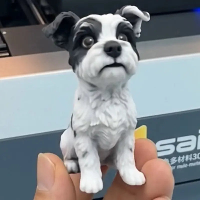 Front view of a full-color 3D figurine of a black and white dog held between two fingers